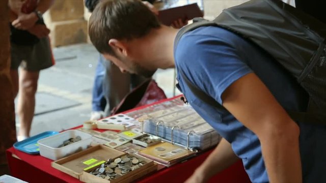 Tourist looking through coins in wooden box on table at street market, travel