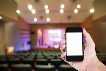 Smartphone on hand and white screen with blurry background of theater.
