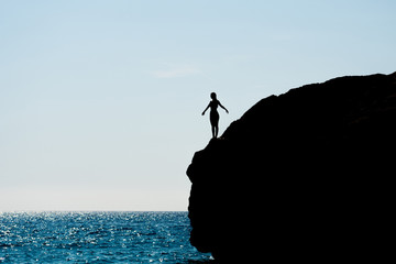 Silhouette of a girl standing on a rock by the sea