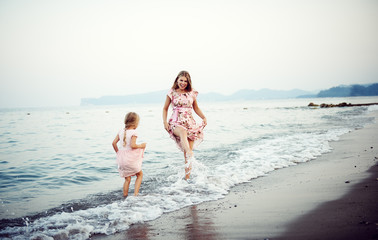 Happy woman with her little daughter in dresses splashing water on the beach. Family summer vacation.