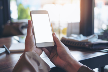 Mockup image of hands holding white mobile phone with blank screen in vintage cafe