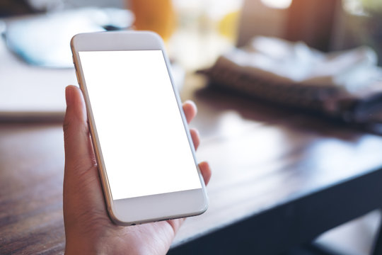 Mockup image of a hand holding white mobile phone with blank screen in vintage cafe