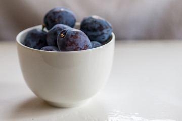 Closeup of a bowl of ripe plums on a white background. Shallow depth of focus. Health concept from nature. Copy space.