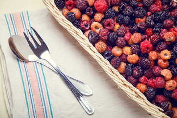 Top view of wild berries in wicker basket on table with spoon and fork