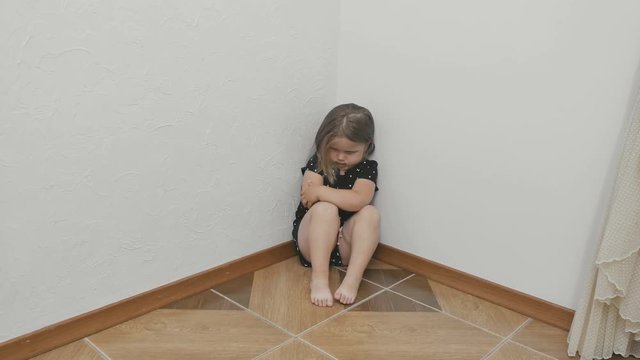 Sad little girl with bruise near the eye sits on the floor and hugs herself