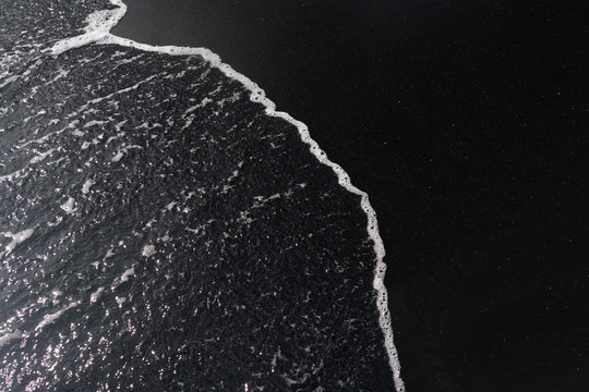 white ocean foam on black sand volcanic texture