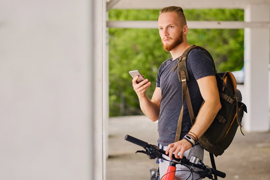 A man sits on a red mountain bicycle and holds a smartphone.