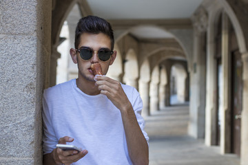 young teenage man with mobile phone and ice cream on city street