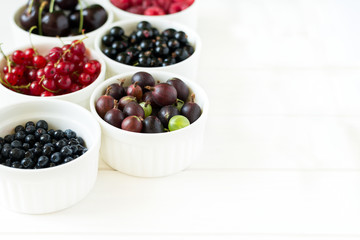  Bowls with fresh ripe gooseberry, red currant, black currant, raspberry, blueberry and cherry on white wooden table