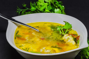 A delicious soup with vegetables and fish on a black background, very healthy healthy food in a white bowl.