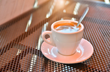White cup of coffee on a metal grated table in a cafe