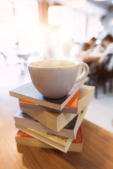A cup of coffee on books stack on the coffee shop table. At the time of university student exams in selective focus.