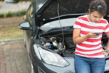 young Asian woman is worried and calling for assistance with her car broken down in selective focus.