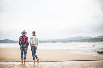 Two girls watching the sea barefoot in the fall season