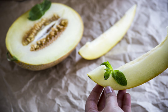 Women's hands hold a melon slice with mint