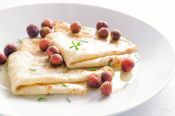 a plate with crepes, garden strawberries, thyme, and honey