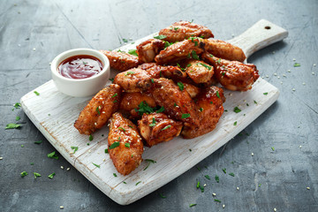 Baked chicken wings with sesame seeds and sweet chili sauce on white wooden board.