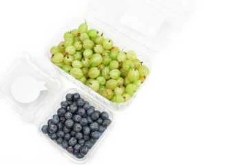 Gooseberry and blueberry in plastic container. Berries in a transparent cups isolated on white background. The harvest in the fall.