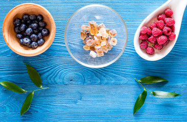 Preparing raspberry jam. Berries and sugar on blue wooden background top view copyspace