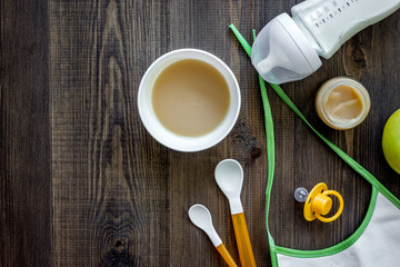 Preparing to feed baby. Puree, spoon, nipple, bottle and bib on dark wooden table background top view copyspace