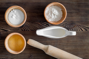 Put the dough. Flour, salt, oil, milk and rolling pin on dark wooden table background top view
