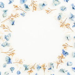 Fototapeta na wymiar Floral round frame made of blue petals and branches on white background. Flat lay. Top view.