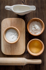 Put the dough. Flour, salt, oil, milk and rolling pin on dark wooden table background top view