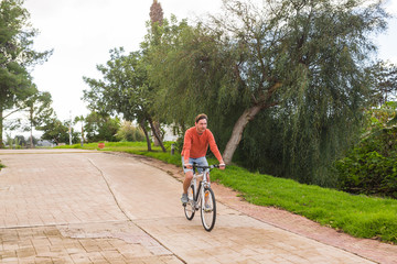 Handsome young man on bike in the park. Bicycle, leisure and people concept.