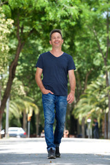 Full length happy man walking outside in park by trees