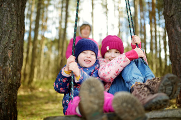Two cute little sisters having fun on a swing together in beautiful autumn forest on warm and sunny day outdoors