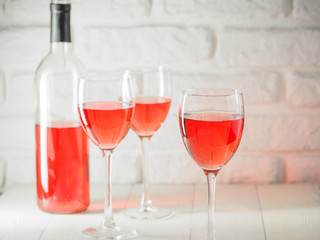 Three wineglass and bottle of pink wine on white brick wall background. Rose wine in wineglass. Copy space.