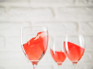 Three wineglass with pink wine on white brick wall background. Splashes rose wine in wineglass. Copy space.