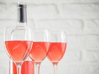 Three wineglass with pink wine and bottle on white brick wall background