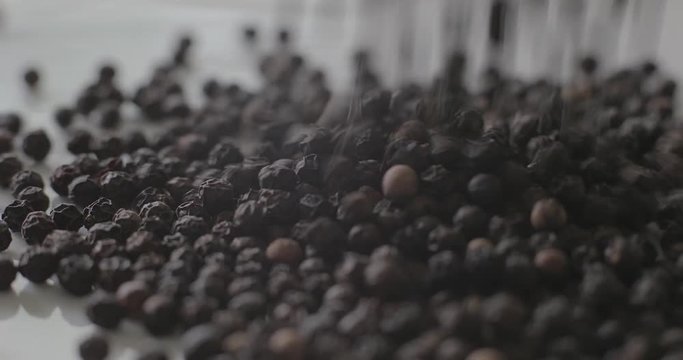 Peppercorns pour onto a white surface, ready for using as a spice for healthy cooking.