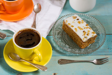 Carrot cake with coffee. Blue wooden table, cristal plate, yellow and orange cup.