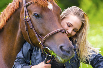 Beautiful woman feeding her arabian horse with grass in the field