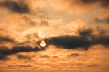 orange sky with smoky clouds at sunset moving over the sun