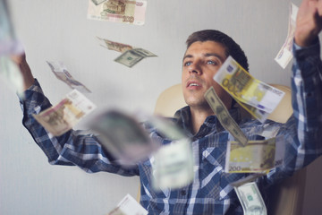 young man businessman among flying banknotes(euros, rubles, dollars)