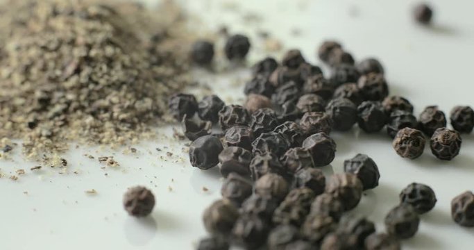 Ground black pepper and whole peppercorns on a white plate, in a pile for using in healthy cooking.