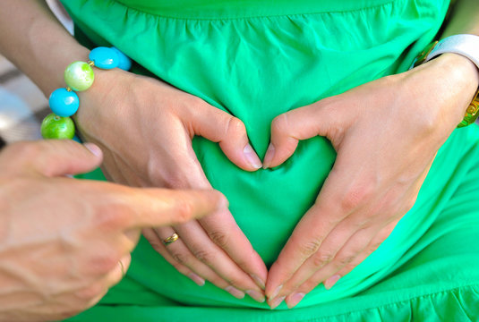 Taking care of your body. The concept of a pregnancy diet. Female hands forming heart shape on belly.