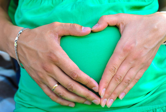 Taking care of your body. The concept of a pregnancy diet. Female hands forming heart shape on belly.