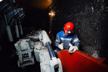 young miner man underground in a mine for coal mining in overalls is busy with work, repairing...