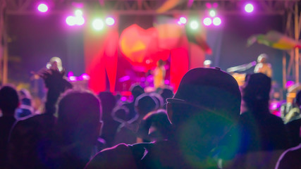 Fototapeta na wymiar Silhouette of man in the crowd in baseball cap on reggae concert bright lights with lens flare
