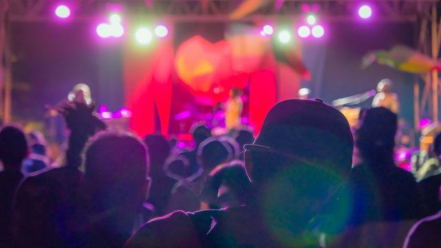 Silhouette of man in the crowd in baseball cap on reggae concert bright lights with lens flare