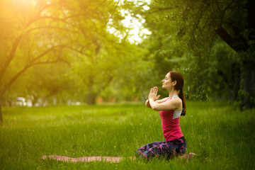 Obraz premium Young female in morning garden practicing yoga in diamond pose. Woman doing vajra-asana, relaxing outdoors. Toned image.