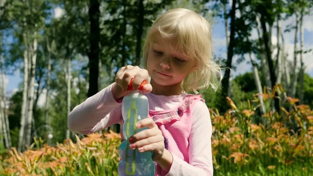 The happy blonde little girl playing with soap bubbles in the summer park. Slow motion. HD