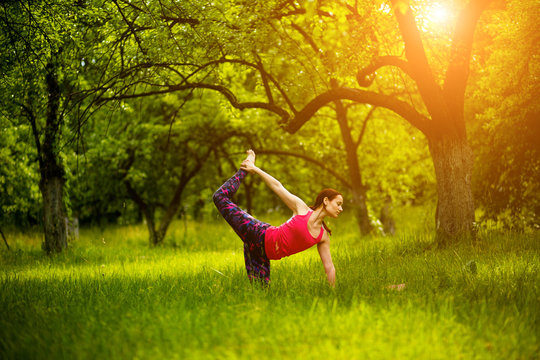 Practicing Yoga Asanas In Nature. Woman Practicing Cat Pose With Leg Seizure. Yoga Pose Marjaryasana. Toned Image.