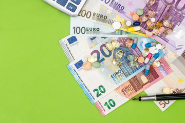 Euro bills with different pills and pen on green