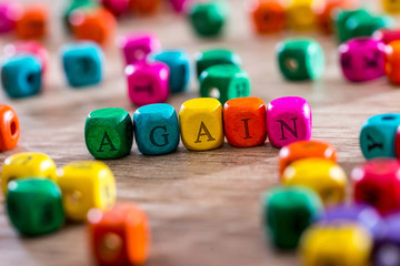 again - word created with colored wooden cubes on desk.