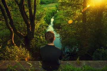 Young man sitting outdoor at the river and looking at the sunrise